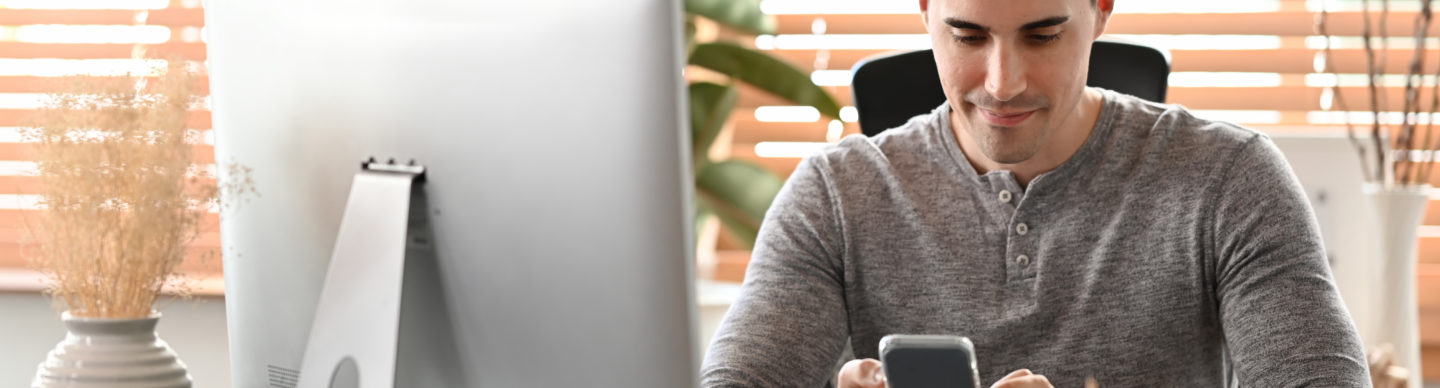 Attractive man sitting at home office and using smart phone.